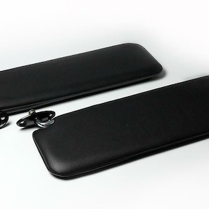Puede incluir: Dos viseras para el sol de coche de cuero negro con soportes de montaje de metal.