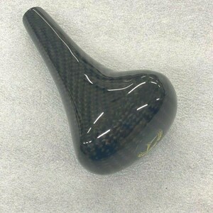 May include: A black carbon fiber gear shift knob with a gold logo.