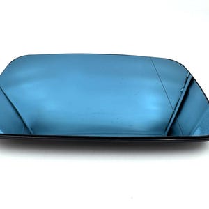 Könnte beinhalten: Ein rechteckiges Auto-Außenspiegelglas mit einer bläulich getönten Spiegelfläche. Das Glas weist nahe dem rechten Rand eine dünne, vertikale schwarze Linie auf, die einen Weitwinkelbereich markiert, und ist von einem schmalen schwarzen Rand umgeben.