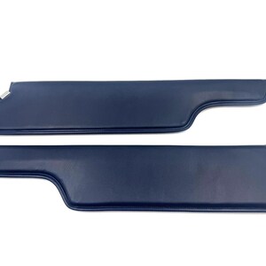 May include: Two navy blue car sun visors. Each visor has a curved shape with a silver metal bracket on one end and a straight metal rod on the other. The visors are made of a smooth, solid material.