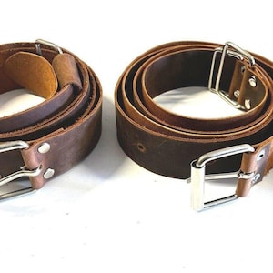 May include: Two brown leather belts with silver buckles. The belts are folded and laid out on a white surface.