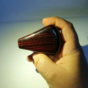 Könnte beinhalten: Ein dunkelbrauner und roter, gestreifter Schaltknauf aus Holz.