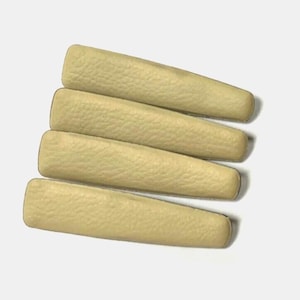 May include: Five beige hair clips, stacked on top of each other. The clips are made of a textured material and have a slightly rounded shape.
