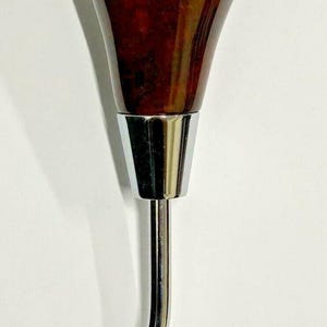 May include: A car gear shift knob with a dark brown, glossy wooden top and a chrome-coloured metal base and stem. The stem is curved and has a threaded end.