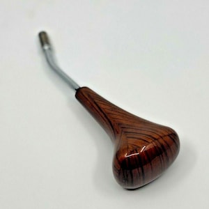 May include: A wooden gear shift knob with a brown and black woodgrain pattern. The knob has a silver metal shaft.