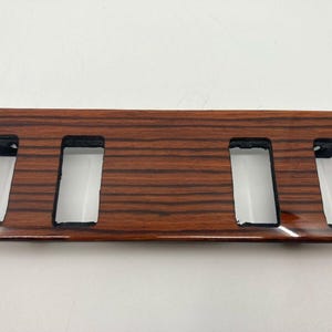 Puede incluir: Una moldura de madera con cuatro recortes rectangulares. La madera tiene un patrón de veta marrón y marrón rojizo.