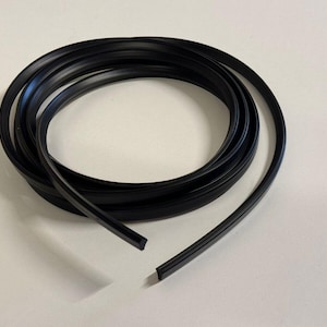 May include: A roll of black rubber weather stripping, possibly for vehicles or building. The material is flexible and appears new, with a smooth surface. The weather stripping is coiled in a circular shape, ready for use.