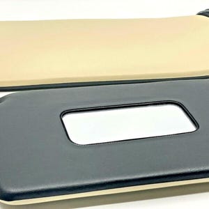 May include: Two car sun visors, one black with a rectangular window and one beige. Both have a black trim.