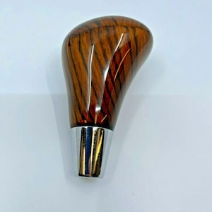 Op de afbeelding: Een houten versnellingspookknop met een bruin en oranje houtnerfpatroon en een chromen basis.