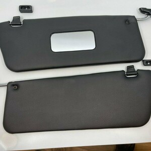 May include: Two black leather car sun visors with a chrome metal frame and a small rectangular mirror on the top visor.