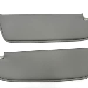 May include: Two gray car sun visors. Each visor has a rounded end and a rectangular metal clip. The visors are made of a smooth, solid gray material and are designed to block sunlight.
