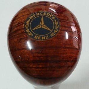 May include: A wooden gear shift knob with a Mercedes-Benz logo in gold and black.