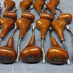 May include: A collection of wooden gear shift knobs with a chrome metal base. The knobs are a rich brown colour with a wood grain pattern. Each knob features a gold logo.