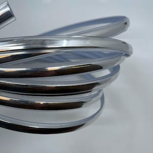 May include: A close-up of a silver trim moulding, showing the shiny, reflective surface. The moulding is rolled up in a coil, revealing the flexible nature of the material.