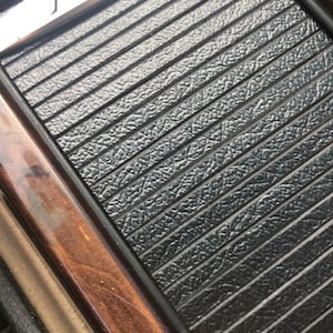May include: Close-up of a black leather-like panel with a silver "ABT Sportline" logo. The panel is surrounded by a wooden frame.