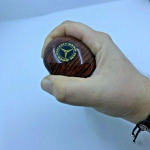 May include: A brown wooden gear shift knob with a black and gold Mercedes-Benz logo.