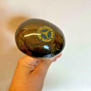 May include: A close-up of a wooden car gear knob with a gold Mercedes-Benz logo.