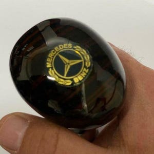 以下が含まれることがあります： 黒い木製のシフトノブに金色のメルセデス・ベンツのロゴが刻まれています