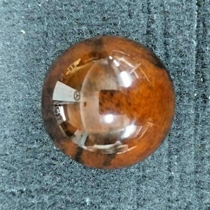 May include: A close-up of a round, brown and orange, glass cabochon with a reflective surface.