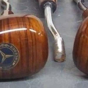 Puede incluir: Cinco pomos de cambio de marchas de madera con un logotipo de estrella en el centro. Los pomos son marrones con un patrón de veta de madera y tienen una base de metal plateado.