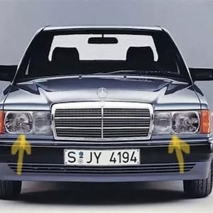 Peut inclure: Vue de face d'une berline argentée classique avec un pare-chocs et une calandre noirs. La voiture a des phares rectangulaires avec des clignotants orange et une plaque d'immatriculation "S:JY 4194". L'emblème Mercedes-Benz est visible sur le capot.