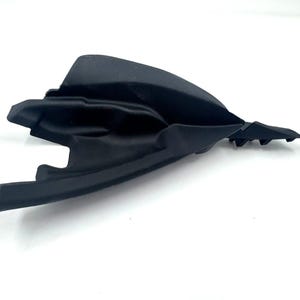 Puede incluir: Un componente de moldura automotriz de plástico negro mate con una forma aerodinámica contorneada, un extremo puntiagudo y pestañas de montaje integradas en el lateral. La pieza tiene una superficie moldeada lisa con pliegues geométricos.