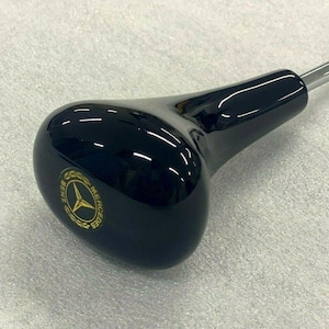 以下が含まれることがあります： 黒いシフトノブに金色のメルセデス・ベンツのロゴが刻まれています。ノブは滑らかで光沢のある素材で作られています。