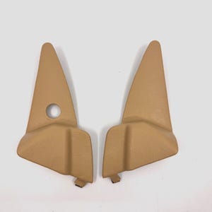 以下が含まれることがあります： ベージュのプラスチック製の車のインテリアトリムパーツ2個。パーツは三角形で、丸みを帯びたエッジと中央に小さな穴があります。