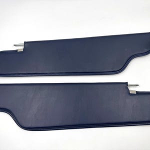 Könnte beinhalten: Zwei marineblaue Autosonnenblenden. Jede Sonnenblende hat eine gebogene Form mit einem abgerundeten Ende und einer Metallstange zur Befestigung. Die Sonnenblenden bestehen aus einem glatten, einfarbigen Material.