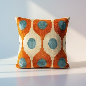 Könnte beinhalten: Quadratisches Zierkissen mit einem geometrischen Muster in Orange, Creme und Türkis. Das Design zeigt ein sich wiederholendes Motiv aus stilisierten Tropfenformen mit türkisfarbenen Kreisen. Das Kissen ist aus einem weichen, strukturierten Stoff gefertigt.