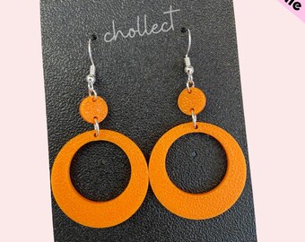 May include: A pair of orange hoop earrings with a smaller circle attached to the top of each hoop. The earrings are on a black card with the word "cholleet" written on it.