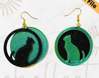 May include: A pair of black and green cat silhouette earrings with gold hooks. The earrings are made of layered circles with a textured surface.