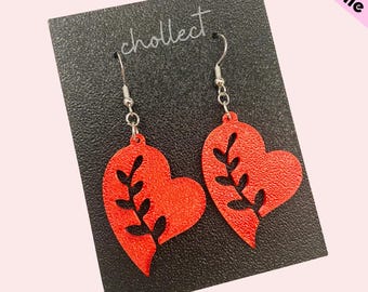 May include: Red heart-shaped earrings with a textured surface and black leaf design. The earrings hang from silver-colored hooks and are displayed on a black card with the word "chollect" printed on it. The words "STL File" are in the upper right corner.