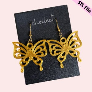 May include: Gold butterfly earrings with a delicate, intricate design. The earrings are on a black card with the word "cholleect" written on it.