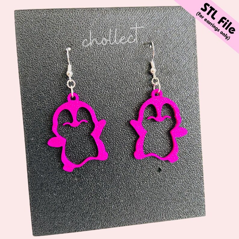 May include: A pair of vibrant pink penguin earrings with silver hooks. The earrings are presented on a dark grey textured surface. The text "STL File (for earrings only)" is in the upper right corner.