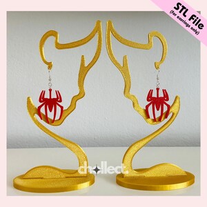 May include: Gold-colored earring display stands holding red spider-shaped earrings. The stands have a unique, artistic design with a circular base and curved upper portion. The text "STL File (for earrings only)" is in the upper right corner.