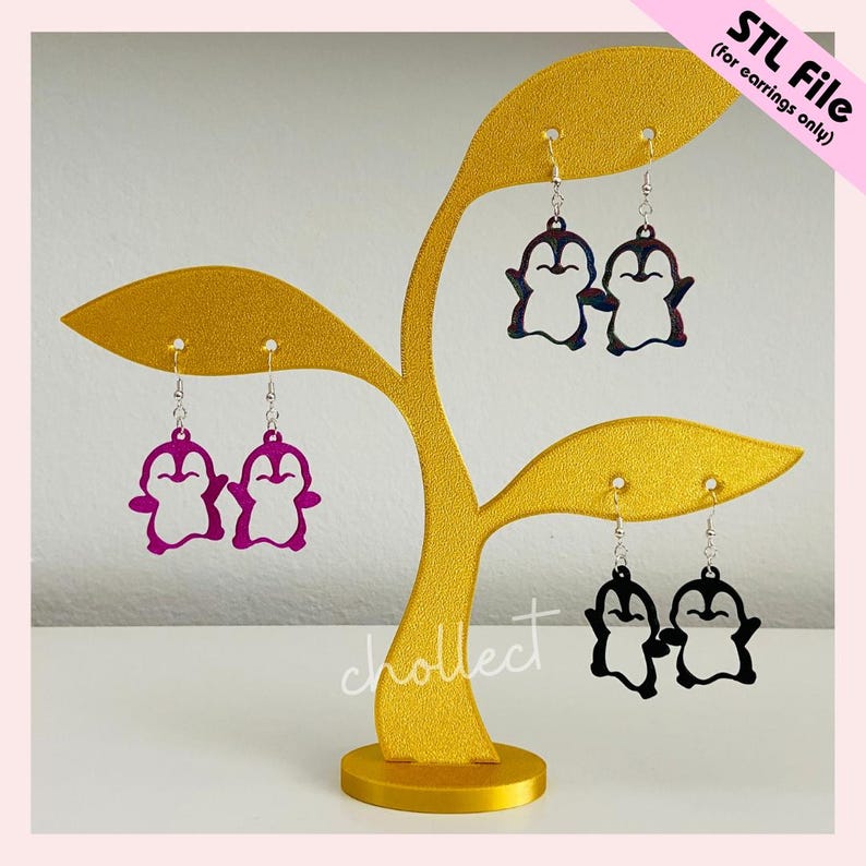 May include: A gold-coloured earring display stand in the shape of a stylised tree, holding several pairs of penguin-shaped earrings. The earrings are in various colours, including purple, black, and a mix of blue and red. Text on the image reads "STL File (for earrings only)."