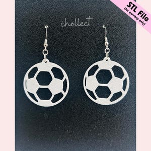 May include: A pair of white soccer ball earrings with a silver hook. The earrings are cut out in the shape of a soccer ball with black pentagons and white hexagons. The word "chollect" is written in cursive.