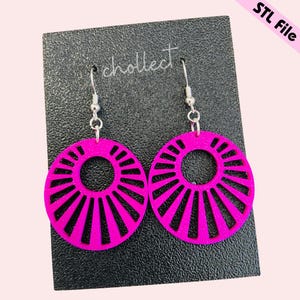 May include: A pair of bright pink, circular earrings with a sunburst design. The earrings are made of a solid material and hang from silver-colored hooks. The earrings are displayed on a black card with the word "chollect" printed on it.