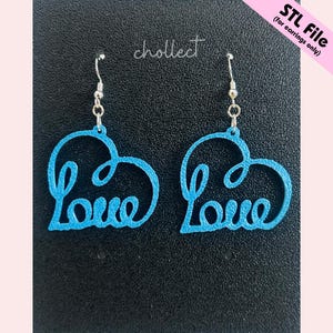 Op de afbeelding: Een paar blauwe hartvormige oorbellen met het woord "Love" in cursief geschreven. De oorbellen hangen aan zilverkleurige haken. De achtergrond is zwart, met de tekst "STL File (for earrings only)" rechtsboven. De merknaam is "chollect".