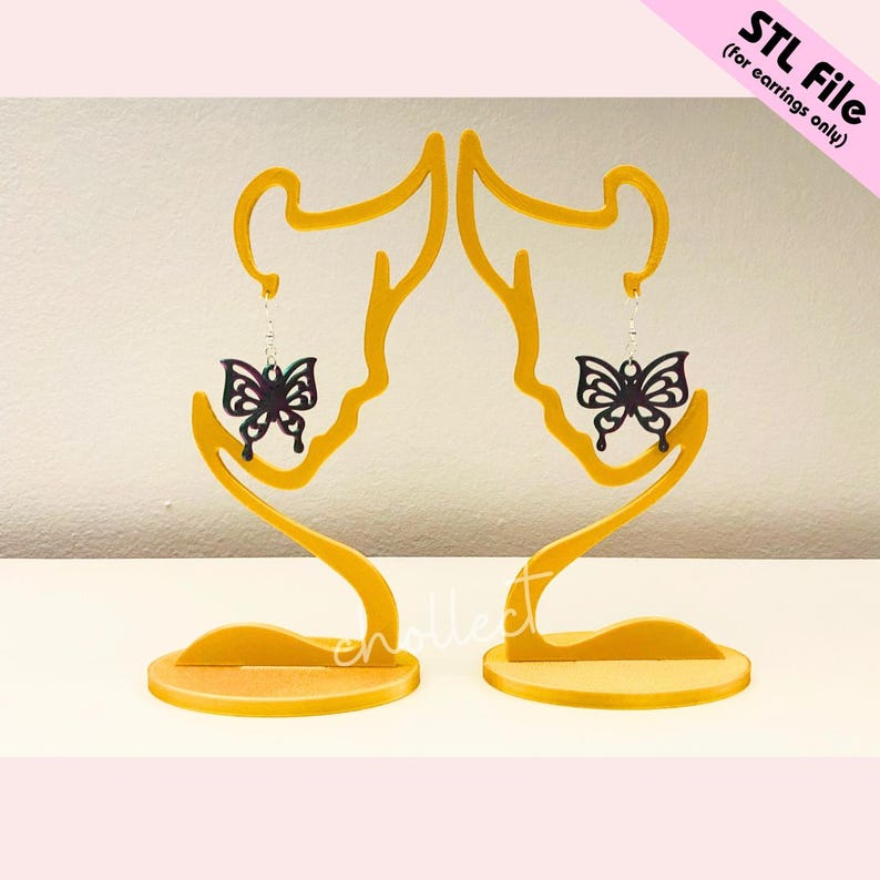 May include: A pair of black butterfly earrings on a gold earring stand. The earrings have a iridescent finish.
