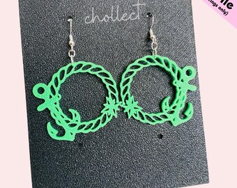 May include: Vibrant green earrings with a nautical theme. Each earring has a circular design with an anchor and a star. The earrings are presented on a black textured surface. The word "chollect" is visible.