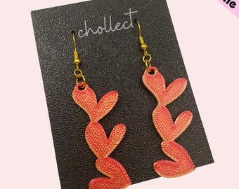 May include: A pair of dangle earrings with a gold hook and a red, textured, heart-shaped design. The earrings are displayed on a black card with the word "cholleect" printed on it.