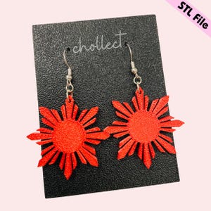 May include: A pair of red star-shaped earrings with silver hooks. The earrings are displayed on a black card with the word "cholleet" printed on it.