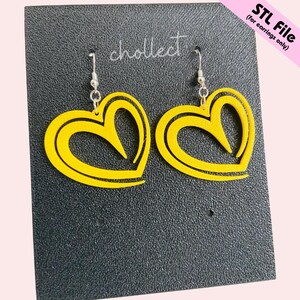 Puede incluir: Un par de pendientes amarillos en forma de coraz&oacute;n con ganchos plateados. Los pendientes est&aacute;n hechos de un material amarillo liso con un contorno negro. Se exhiben sobre una superficie negra con el texto "chollect" y "STL File (for earrings only)".