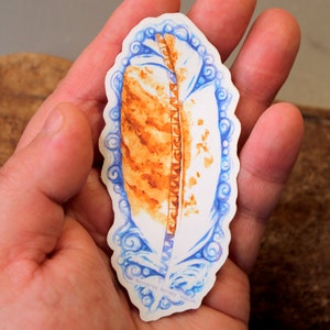 May include: A sticker featuring a watercolor illustration of a brown feather with blue and white swirls around it. The sticker is signed "Masugrac Bailey Hobson".