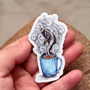 May include: A blue coffee mug with a whale-shaped steam cloud rising from the top. The whale is black and white and is drawn in a whimsical style.