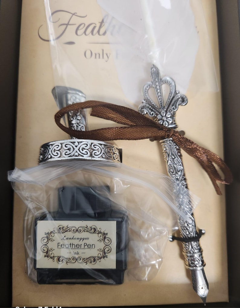 May include: A vintage-style calligraphy set featuring a silver-colored pen with ornate detailing, a matching inkwell, and a bottle of ink. The ink bottle has a label that reads "Lankongyue Feather Pen". The set is packaged in a box.