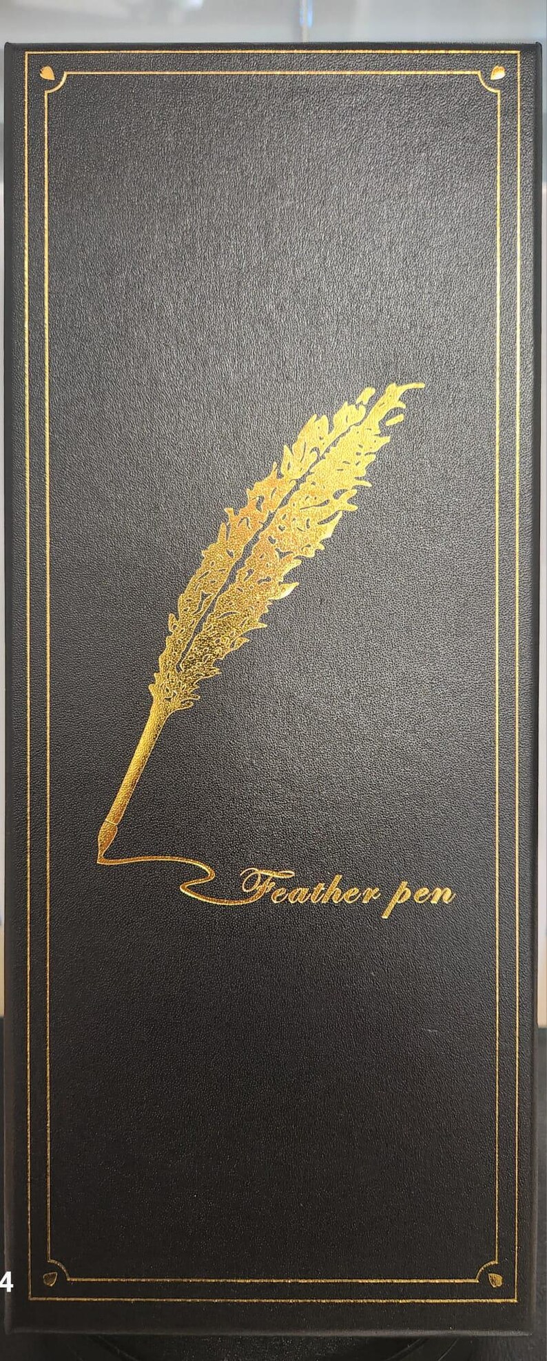 May include: Black box with a gold border and a gold feather pen design. The words "Feather pen" are written in gold script below the feather. The box has a textured surface.