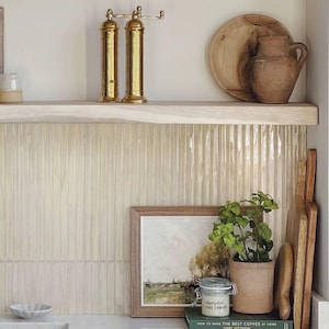 Könnte beinhalten: Ein Küchenregal zeigt Messing-Pfeffermühlen, einen Holzteller und einen Tonkrug. Darunter sind ein gerahmtes Landschaftsbild, eine Topfpflanze und ein Glas Fine Tomato angeordnet. Holzschneidebretter lehnen an der Wand, was eine rustikale Ästhetik erzeugt.